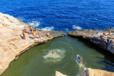 Bir grup insan yeşil bir havuzda yüzüyor. Sahne canlı ve eğlenceli, çünkü insanlar suyun içinde eğleniyorlar. 6 Ağustos 2024 Giola Thassos Yunanistan.