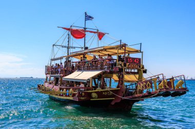 Kırmızı yelkenli ve beyaz tenteli büyük bir tekne okyanusta yüzüyor. Tekne insan kaynıyor ve teknede birkaç bayrak var. 8 Ağustos 2024 Selanik Yunanistan