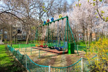Salıncaklı ve çitli bir park. Salıncak yeşil renge ve mavi ve kırmızı renge sahiptir. 1 Nisan 2024 Balti Moldova