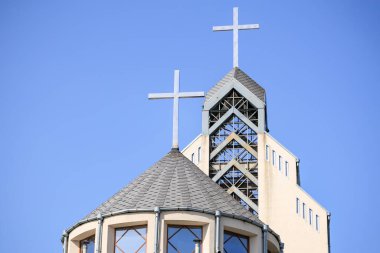 Açık mavi gökyüzüne karşı haçlar bulunan modern kilise mimarisi.
