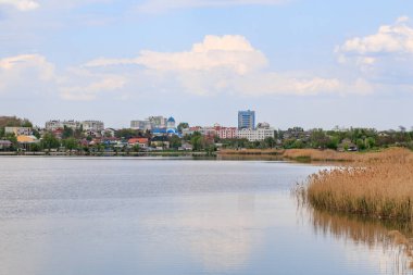 Sakin göl manzarası bulutlu gökyüzünün altında uzak şehir silueti.