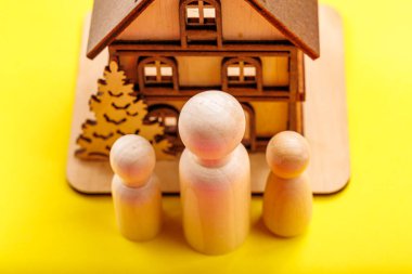 Tahta figürler ve sarı arka planda ev modeli..