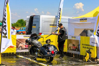 Bir motorcu, motosikletini dışarıdaki temizlik kabininde temizlemek için güçlü bir basınç makinası kullanır. Etkili araç temizleme ürünleri gösteriliyor. 2 Temmuz 2023 Liadoveni Moldova.