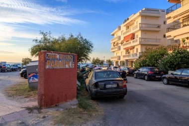 Kırmızı tuğlalı bir duvarda bir park işareti var. Tabela yolun kenarına park edilmiş bir arabanın önündedir. 8 Ağustos 2024 Perea Yunanistan