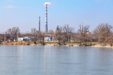 Endüstriyel bacalar, donmuş nehir ve kışın çıplak ağaçlar. 22 Şubat 2025 Balti Moldova.