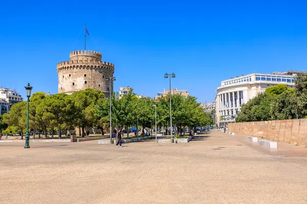 Arkasında büyük bir kule olan bir şehir meydanı. Gökyüzü açık ve mavi. Meydanın etrafında yürüyen birkaç kişi var. 8 Ağustos 2024 Selanik Yunanistan