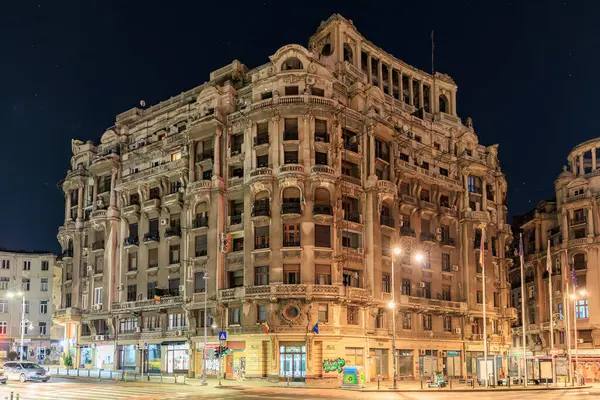 Geceleri aydınlatılmış pencereleri ve sokak lambaları olan tarihi mimari bir bina. 8 Mart 2025 Bükreş Romanya.