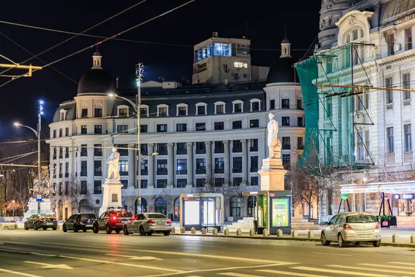 Aydınlatılmış heykelleri ve trafiği olan tarihi şehir mimarisinin gece manzarası. 8 Mart 2025 Bükreş Romanya.