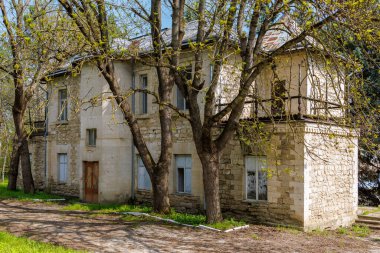 Terk edilmiş taştan bir ev, sakin bir ortamda yapraklı ağaçlarla çevrili..