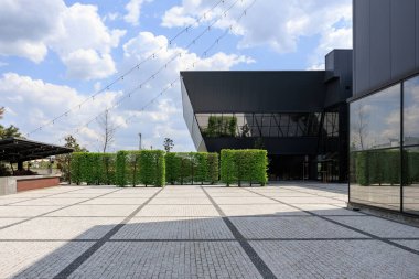 Mavi gökyüzünün altındaki şehir meydanında modern mimari ve yeşillik.