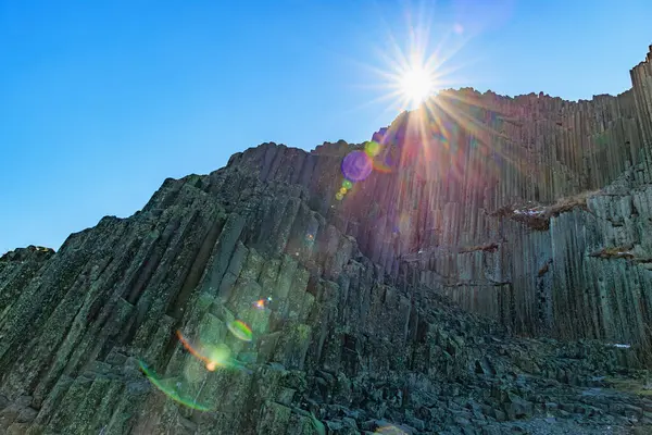 Parlak mercekli güneş ışığı bazalt sütunları açık mavi gökyüzüne karşı parlıyor.