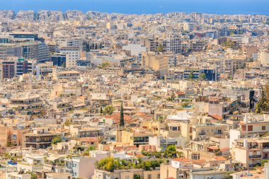 Arka planda büyük bir su kütlesi olan bir şehir manzarası. Şehir yüksek binalarla dolu ve etrafta dolaşan bir sürü insan var. Sahne meşgul ve hareketli. 9 Ağustos 2024 Atina Yunanistan