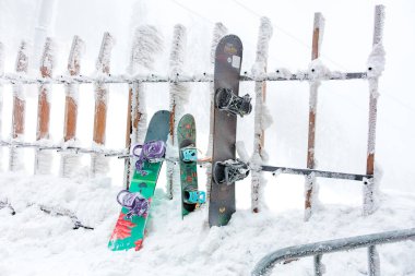 Kar kaplı snowboardlar kış günü buz gibi bir çitin önünde dinleniyor. 15 Aralık 2024 'te Romanya.