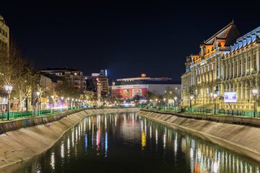 Bükreş 'in Dambovita Nehri' nin gece manzarası, aydınlık binalar ve şehir manzarasıyla Romen nehrinden tercüme ediliyor. 8 Mart 2025 Bükreş Romanya.