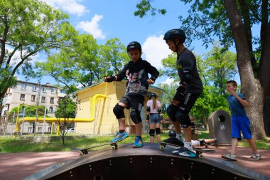 Parkta kaykay yapan beyaz çocuklar koruyucu giysiler giyiyorlar. 31 Mayıs 2024 Balti Moldova.