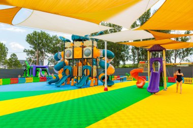 Büyük bir kaydırak ve oyun yapısı olan bir oyun alanı. Bir kadın oyun alanının yanından geçiyor. Oyun alanı renkli ve davetkar. 8 Haziran 2024 Balti Moldova