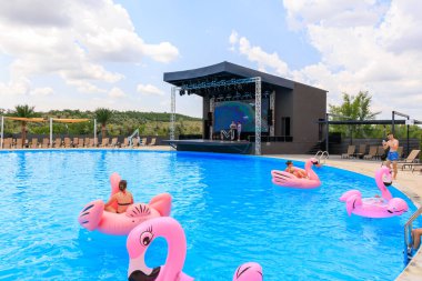 Bir grup insan havuzda şişme flamingo şeklinde yüzüyorlar. Havuz bir sahne ile çevrili ve bir kalabalık gösteriyi izliyor. 8 Haziran 2024 Balti Moldova