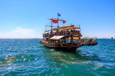 Kırmızı yelkenli ve beyaz tenteli büyük bir tekne okyanusta yüzüyor. Tekne insan kaynıyor ve teknede birkaç bayrak var. 8 Ağustos 2024 Selanik Yunanistan