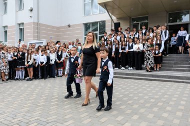 Beyaz kadın ve iki genç çocuk okul töreninde etrafı öğrencilerle çevrili. 2 Eylül 2024 Balti Moldova.