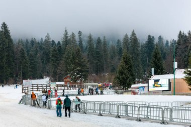 Bulutlu bir günde insanlarla ve yemyeşil ağaçlarla dolu karlı bir dağ evi. 15 Aralık 2024 'te Romanya.