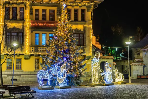 İçinde bir adam ve iki kadın olan bir Noel ağacı ışıldıyor. Sahne sarı cepheli bir binanın önünde geçiyor. 13 Aralık 2024 Brasov Romanya