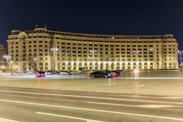Geceleri büyük tarihi binalar ve park edilmiş arabalarla aydınlatılmış şehir meydanı. 8 Mart 2025 Bükreş Romanya.