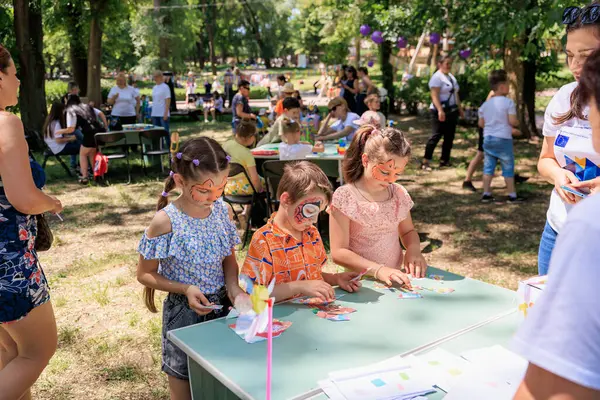 Bir grup çocuk piknik masasında kağıt ve makasla oynuyorlar. Sahne eğlenceli ve eğlenceli. 1 Haziran 2024 Balti Moldova.