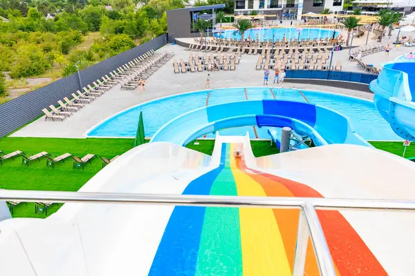 Üzerinde gökkuşağı olan renkli bir kaydırak bir su parkında. Kaydırak sandalyeler ve diğer dinlenme odaları ile çevrilidir. 8 Haziran 2024 Balti Moldova