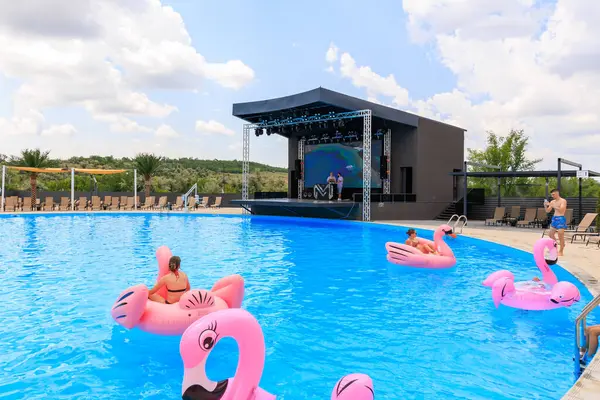 Bir grup insan havuzda şişme flamingo şeklinde yüzüyorlar. Havuz bir sahne ile çevrili ve bir kalabalık gösteriyi izliyor. 8 Haziran 2024 Balti Moldova