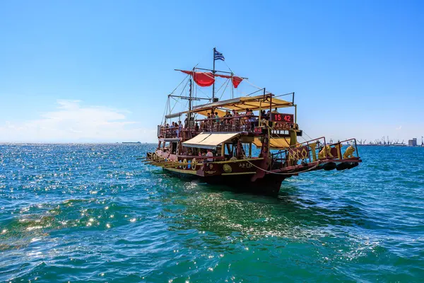 Kırmızı yelkenli ve beyaz tenteli büyük bir tekne okyanusta yüzüyor. Tekne insan kaynıyor ve teknede birkaç bayrak var. 8 Ağustos 2024 Selanik Yunanistan