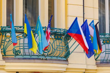 Avrupa şehir merkezindeki sarı binanın balkonunda uluslararası bayraklar.