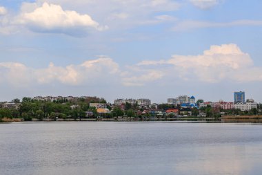 Bulutlu gökyüzü ve uzak binalarla sakin göl kenti manzarası.