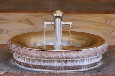 Taş havzadaki çift ağızlı metal su çeşmesi..