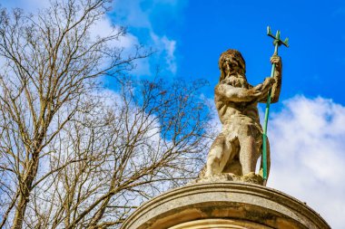 Tarihi neptün heykeli tarihi park ortamında mavi gökyüzüne karşı mızrak tutuyor.