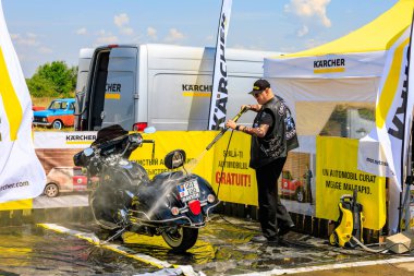 Bir motorcu, motosikletini dışarıdaki temizlik kabininde temizlemek için güçlü bir basınç makinası kullanır. Etkili araç temizleme ürünleri gösteriliyor. 2 Temmuz 2023 Liadoveni Moldova.