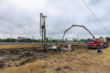 Bulutlu bir günde sondaj kulesi, işçiler ve kamyonlarla inşaat alanı. 25 Haziran 2024 Balti Moldova