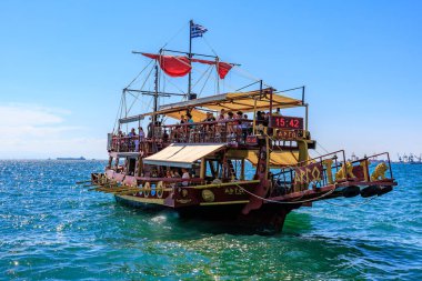 Kırmızı yelkenli ve beyaz tenteli büyük bir tekne okyanusta yüzüyor. Tekne insan kaynıyor ve teknede birkaç bayrak var. 8 Ağustos 2024 Selanik Yunanistan