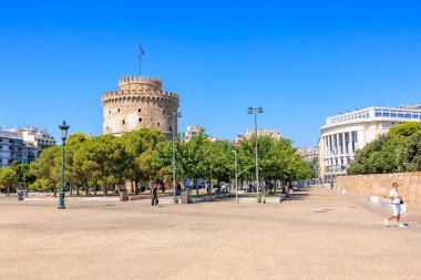 Arkasında büyük bir kule olan bir şehir meydanı. Gökyüzü açık ve mavi. Meydanın etrafında yürüyen birkaç kişi var. 8 Ağustos 2024 Selanik Yunanistan