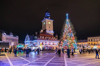 Meydanın ortasında büyük bir Noel ağacı parlıyor. İnsanlar etrafında toplanmış, neşeli atmosferin tadını çıkarıyorlar. 13 Aralık 2024 Brasov Romanya