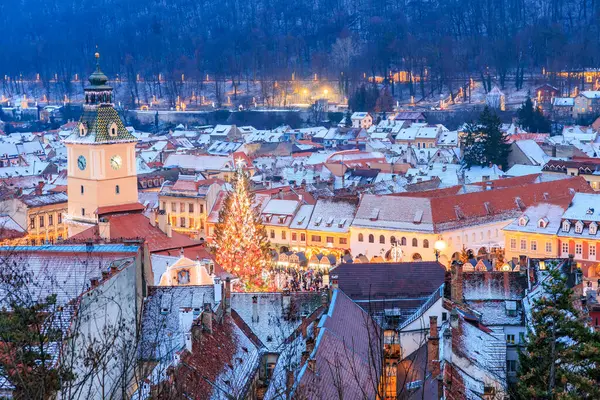 Geceleri ortasında saat kulesi olan bir şehir. Şehir karla kaplı ve Noel ağacı ışıl ışıl. 14 Aralık 2024 Brasov Romanya