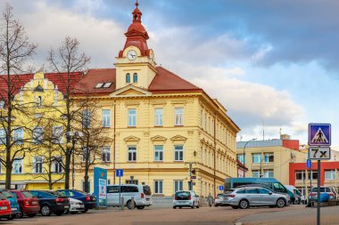 Sokak ve arabalarla şehir merkezinde saat kulesi olan tarihi sarı bina. 17 Mart 2025, Benesov, Çek Cumhuriyeti.