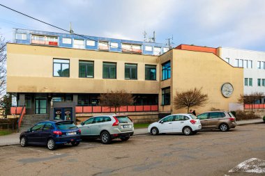 Bulutlu bir günde banliyö ofis binasında saat ve park etmiş arabalar. 17 Mart 2025, Benesov, Çek Cumhuriyeti.