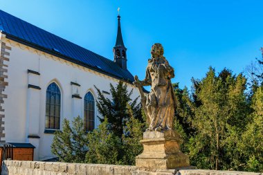 Güneşli bahçe ortamında tarihi heykel ve kilise. 16 Mart 2025, Hruba Skala Şatosu, Çek Cumhuriyeti.