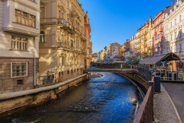 Aydınlık ve güneşli bir günde tarihi şehir ortamında Avrupa nehir kenarını büyülemek. 18 Mart 2025, Karlovy Vary, Çek Cumhuriyeti.