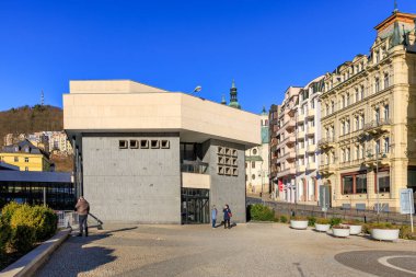 Güneşli bir günde insanların yürüdüğü Avrupa şehir caddesindeki modern mimari binası. 18 Mart 2025, Karlovy Vary, Çek Cumhuriyeti.