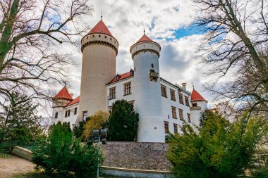 Yeşillik ve bulutlu gökyüzü ile çevrili kırmızı taretleri olan tarihi Avrupa şatosu. 17 Mart 2025, Konopiste Şatosu, Çek Cumhuriyeti.