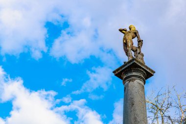 Mavi gökyüzüne ve bulutlara karşı sütun üzerinde antik taş heykel. 17 Mart 2025, Konopiste Şatosu, Çek Cumhuriyeti.