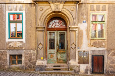 Kemerli ahşap kapılı ve renkli pencere çerçeveli klasik taş bina cephesi. 18 Mart 2025, Madalyon, Çek Cumhuriyeti.