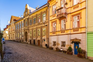 Renkli cepheleri ve güneş ışığında kaldırım taşı yolu olan tarihi Avrupa caddesi. 18 Mart 2025, Madalyon, Çek Cumhuriyeti.