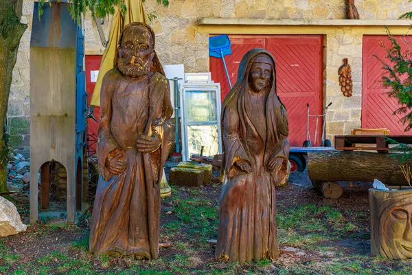 Açık hava ortamında yaşlı beyaz erkek ve kadın figürlerinin kırsal ahşap heykelleri. 16 Mart 2025, Hruba Skala Şatosu, Çek Cumhuriyeti.